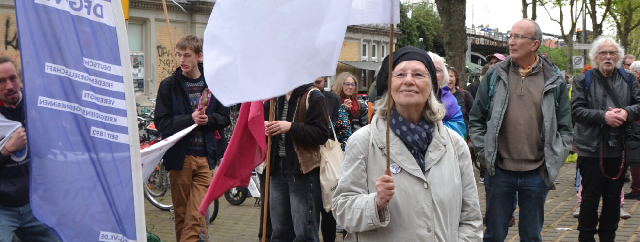 Eine fröhlich schauende ältere Dame mit einer weißen Flagge vor einer Gruppe Menschen